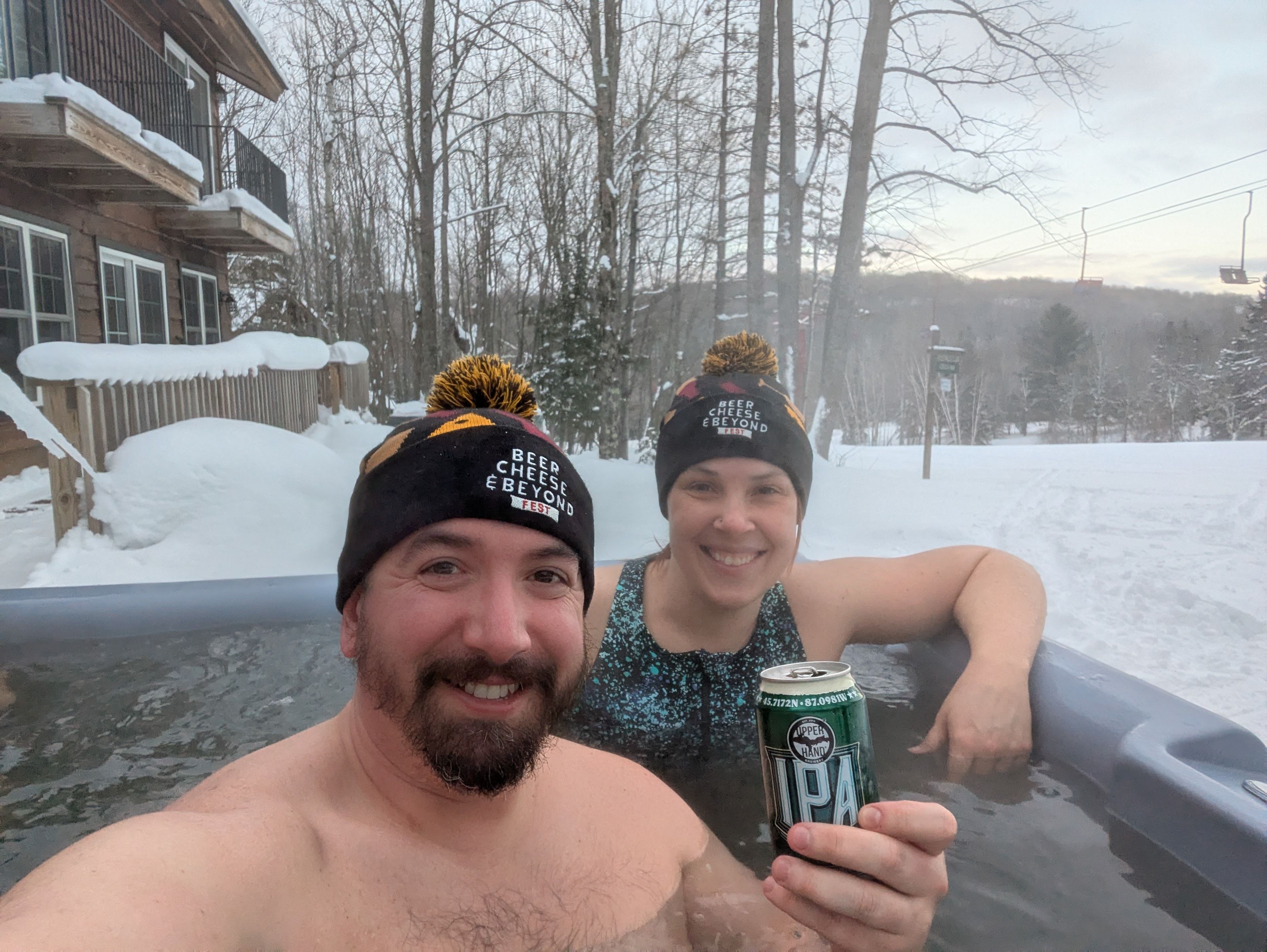 A man and woman in a hotub during winter. The man is holding a beer can.