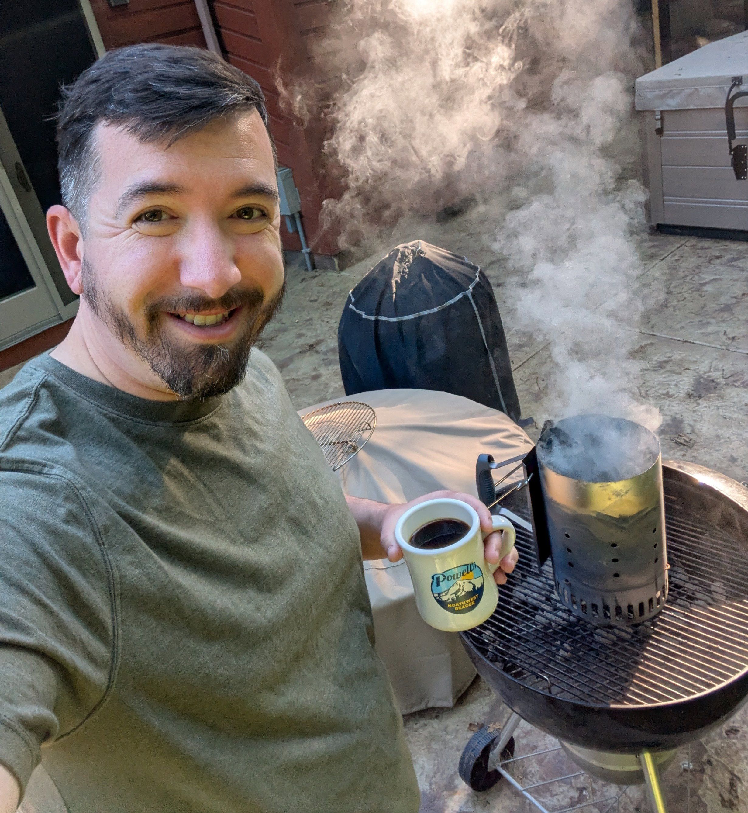 A man on the left holding a coffee mug with charcoal smoking in chimney in the background.